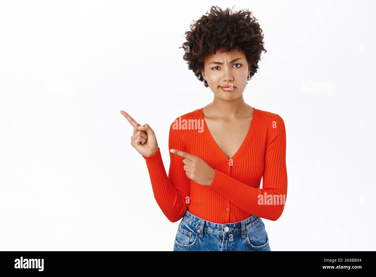 Bella ragazza con sconvolto, faccia delusa, puntando il dito a sinistra, mostrando pubblicità, lamentandosi di smth, in piedi su sfondo bianco Foto Stock