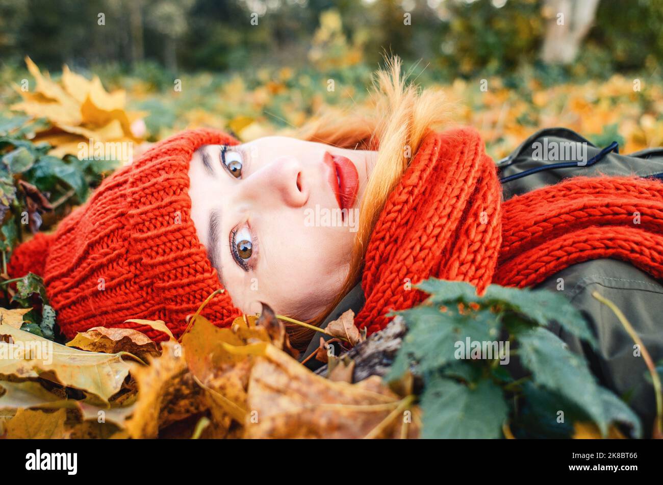 Ritratto autunnale di ragazza carina in caldo cappello a maglia arancione e sciarpa arancione giacente in foglie gialle cadute nel parco. Foto Stock