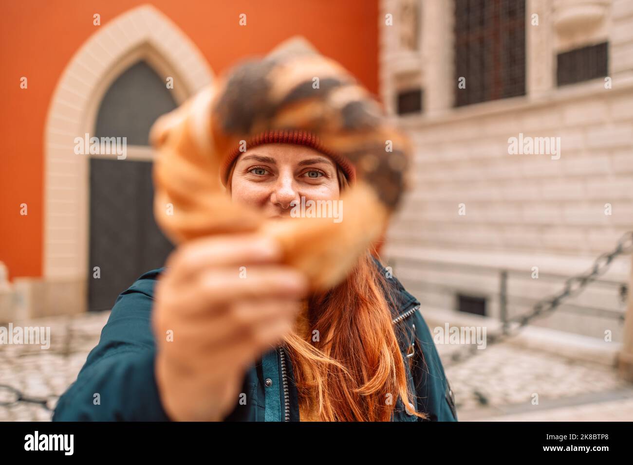 Felice donna turista in un cappello luminoso e giacca autunnale con cotto obwarzanek tradizionale cucina polacca snack bagel sulla piazza del mercato della città vecchia in Foto Stock