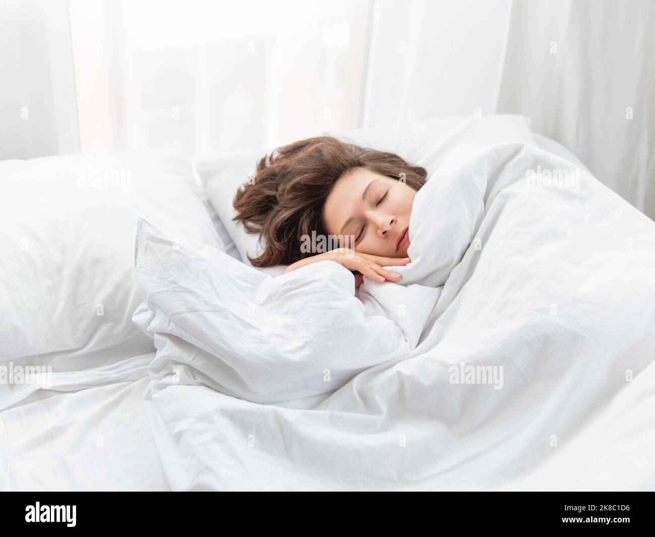 Donna caucasica dorme a letto. Sonno sano sulla biancheria da letto bianca. Mattina a casa accogliente. Foto Stock