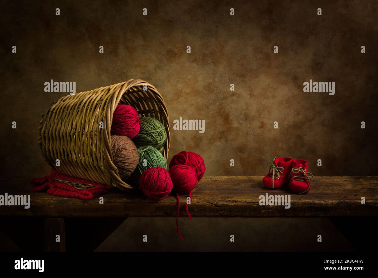 Vecchio cesto di vimini con palle di lana rosse e verdi su una vecchia mensola rustica di legno. Questo è adatto per la composizione digitale. Foto Stock