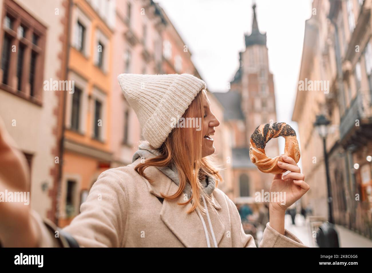 Felice giovane bionda turista in abiti alla moda con pretzel obwarzanek sulla piazza del mercato a Cracovia in Polonia Foto Stock