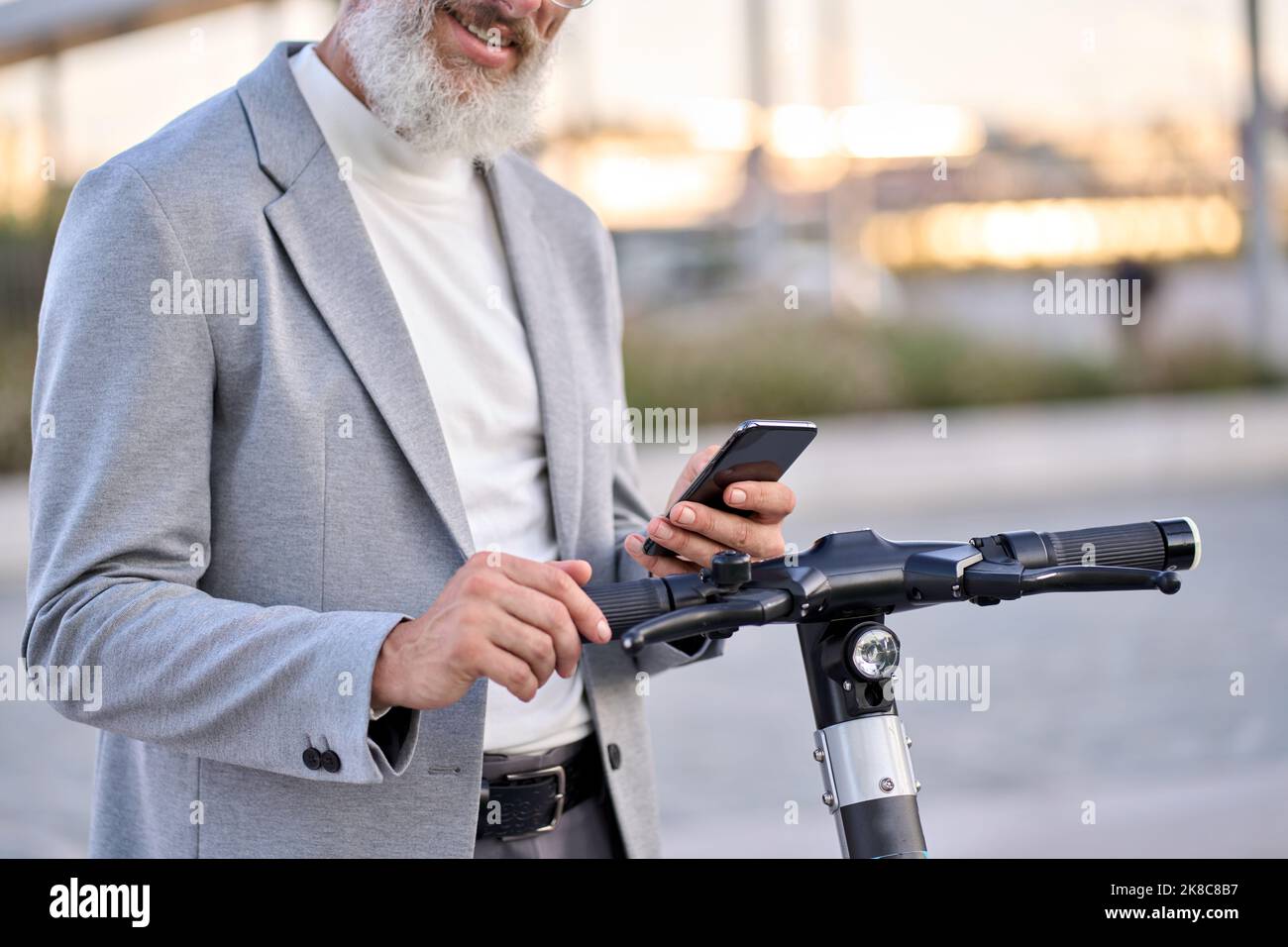Anziano che utilizza l'app mobile per il noleggio di biciclette nel parco cittadino. Foto Stock