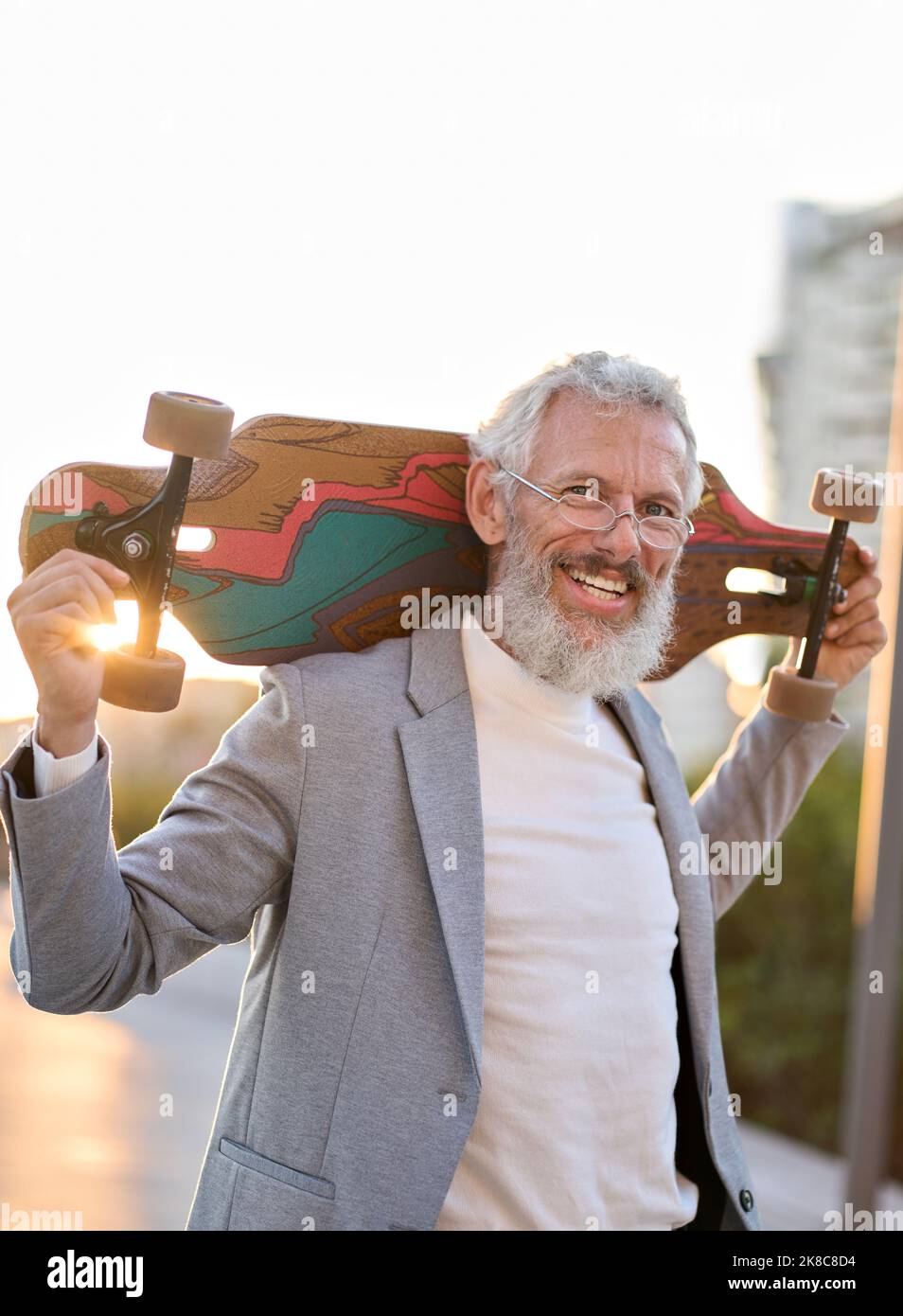 Attivo felice cool vecchio skater uomo d'affari che tiene skateboard in città. Foto Stock