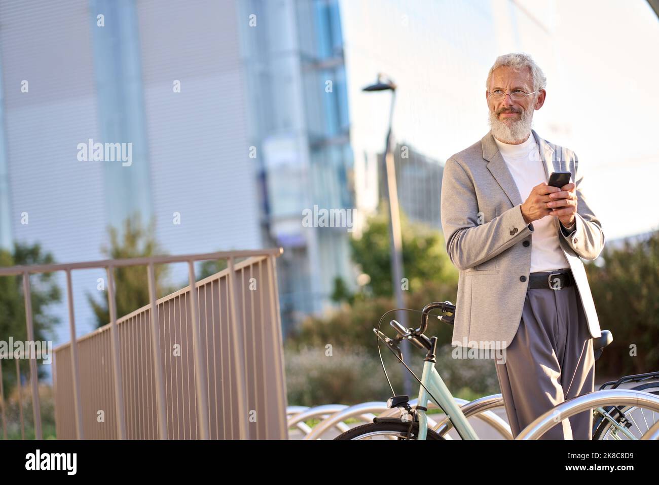 Vecchio uomo anziano che utilizza l'app mobile per il noleggio di biciclette nel parco cittadino. Foto Stock