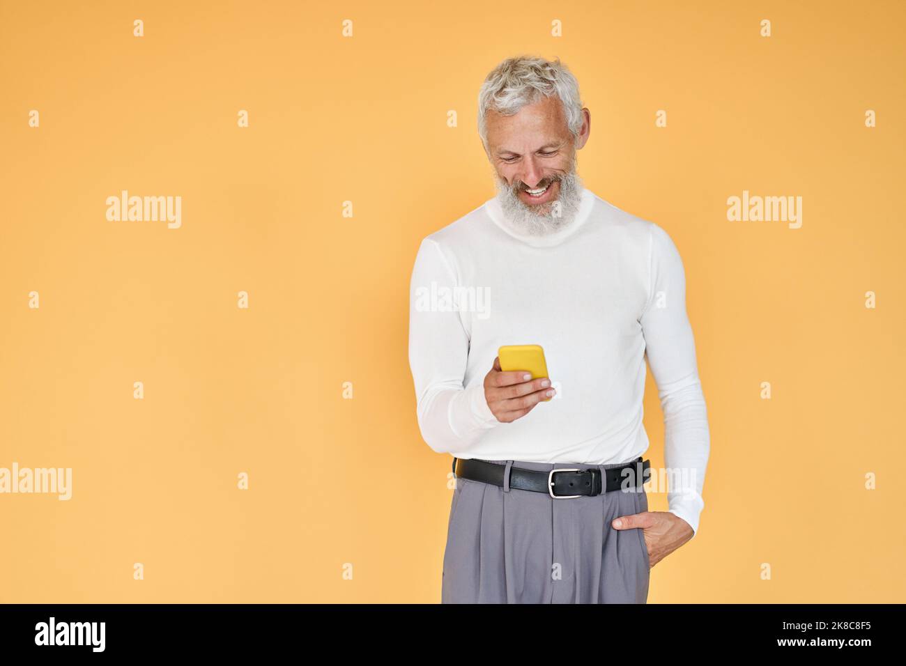 Felice vecchio uomo d'affari senior utilizzando il telefono cellulare in piedi isolato sul giallo. Foto Stock