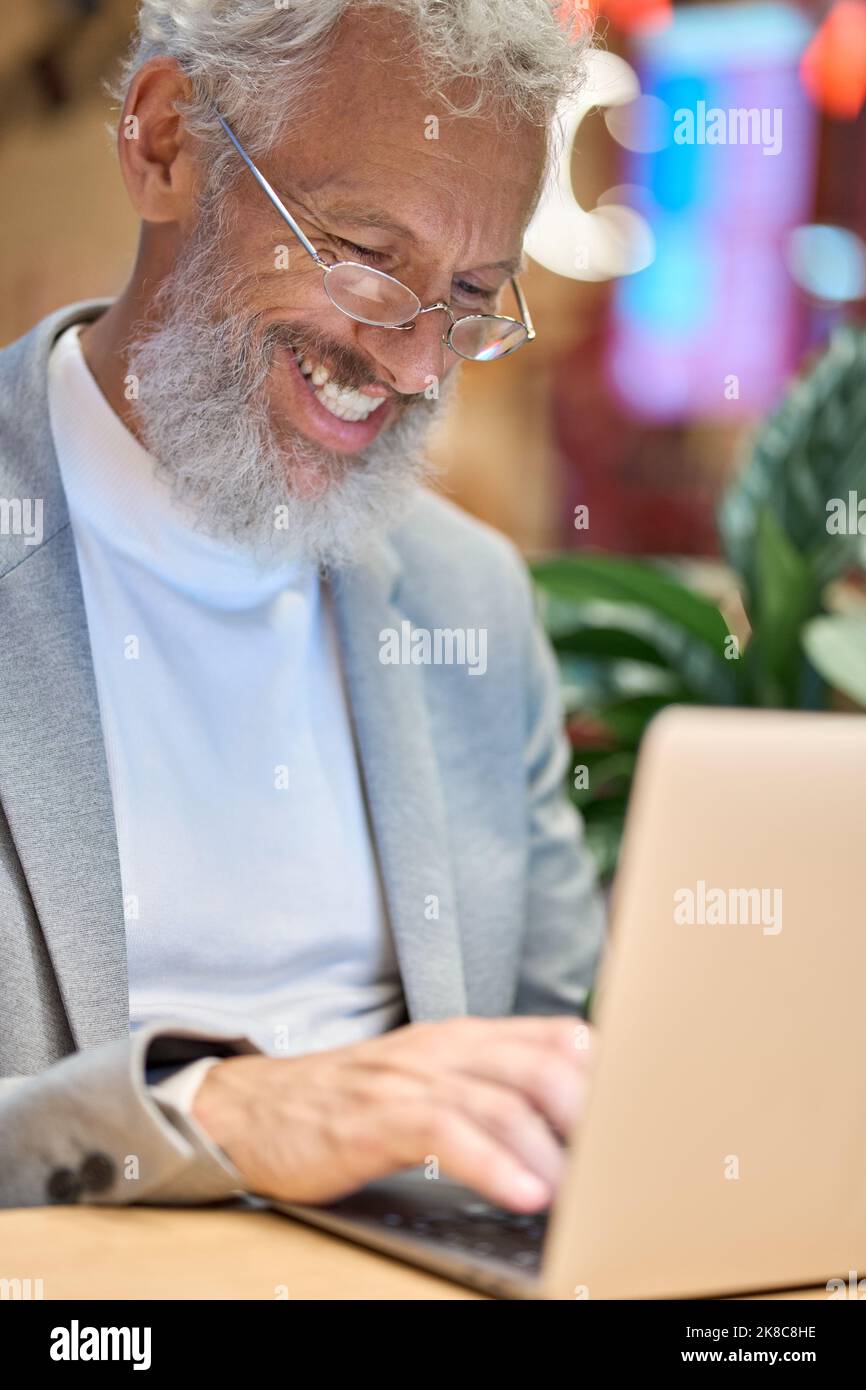 Felice uomo d'affari anziano che utilizza un notebook che lavora tardi sul computer. Foto Stock