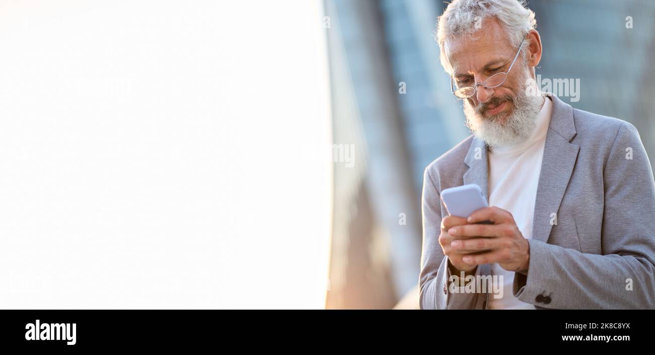 Uomo d'affari professionale più anziano che tiene il telefono usando lo smartphone all'aperto. Foto Stock
