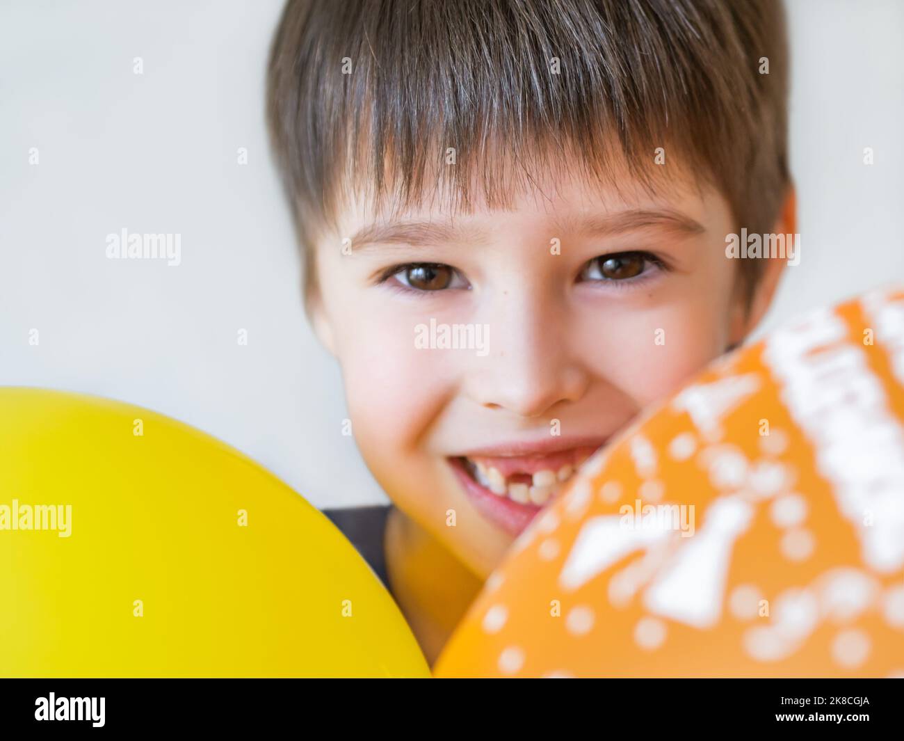 Il ragazzo sorridente mostra un buco in fila di denti in bocca. Un incisor è caduto fuori appena ora. Bambino felice con aerostati. Foto Stock