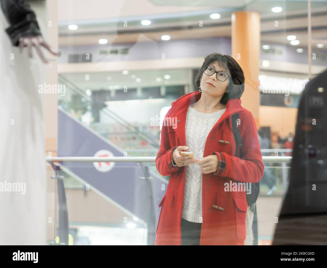 Donna fissa i manichini nel negozio di abbigliamento. Abito casual appeso ai manichini. Visualizza attraverso la finestra trasparente del negozio. Shopping al centro commerciale. Vestiti di base Foto Stock