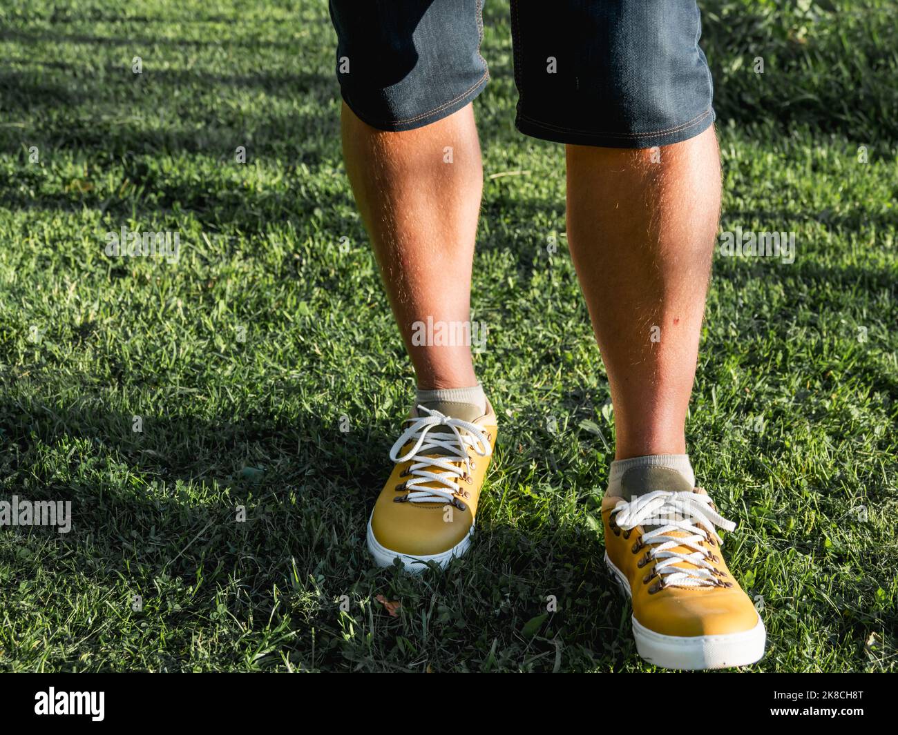 Uomo in sneakers giallo brillante è in piedi su prato verde erba nel parco. Scarpe da hipster moderne. Moda urbana. Foto Stock