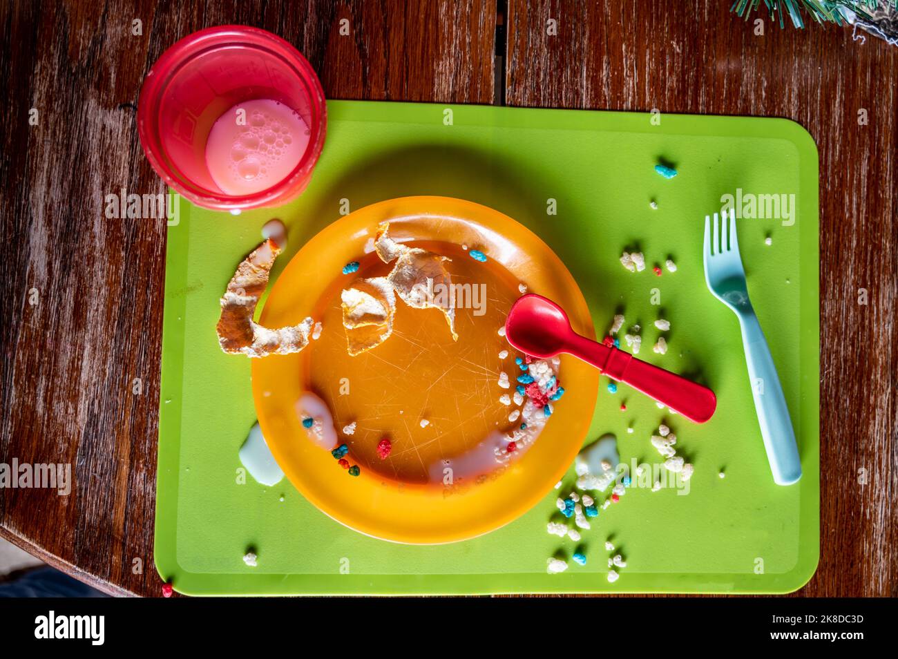 Il disordine ha lasciato al tavolo della cucina dopo che un bambino ha rifinito. Forchetta, tazza e piatto in plastica cosparsi di gocce e briciole. Foto Stock