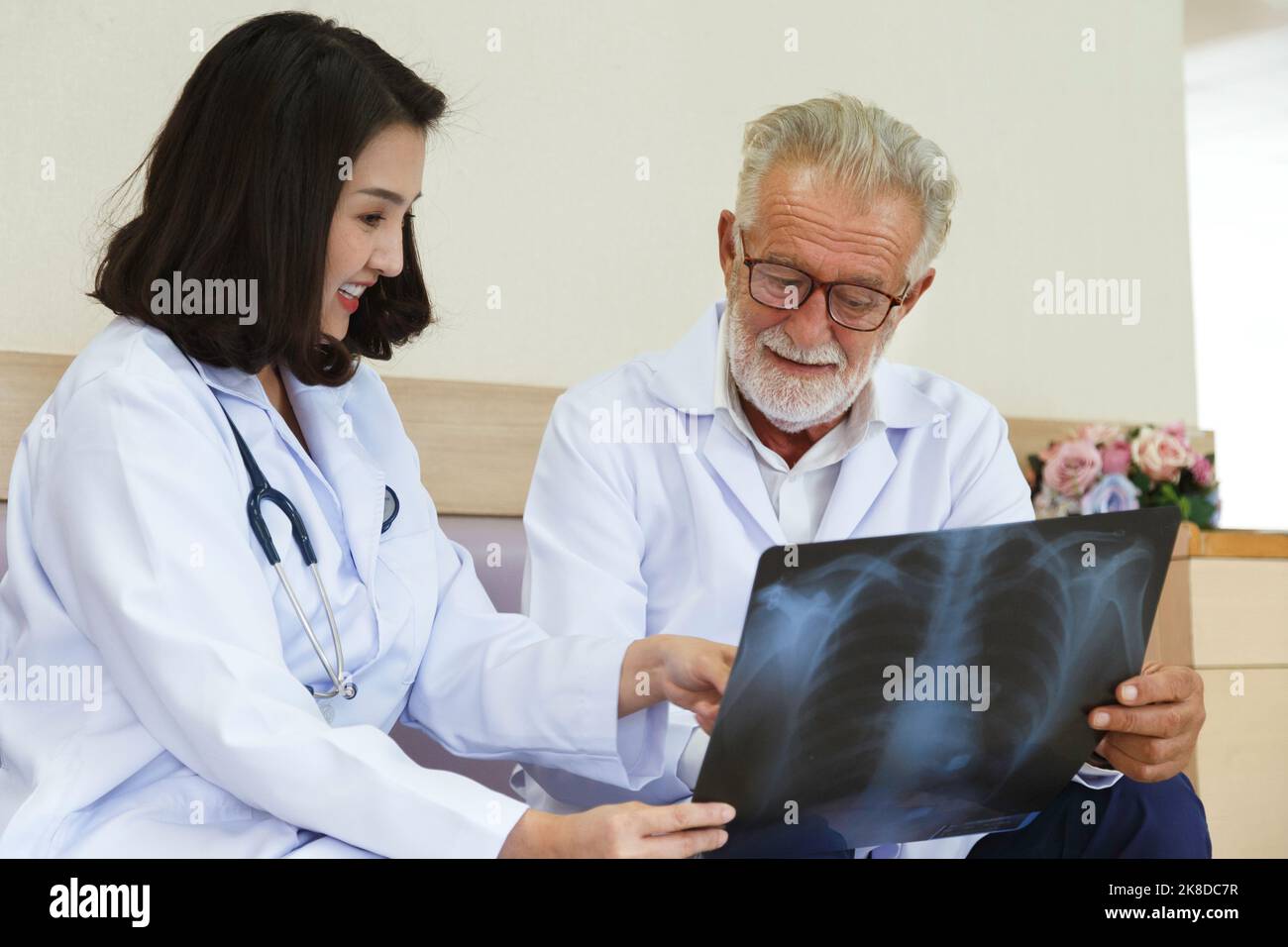 esperienza chirurgico senior guardando la pellicola radiologica per dare consulto e discutere per il trattamento chirurgico il paziente con giovane medico asiatico donna in hos Foto Stock