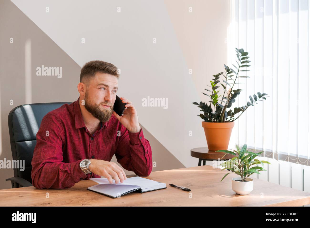 L'uomo affollato di affari sta parlando al telefono e programmi per incontrarsi giornalmente e scrivere un viaggio di affari in un diario sulla scrivania dell'ufficio. Pianificatori di pianificazione del calendario e promemoria del programma. Foto Stock