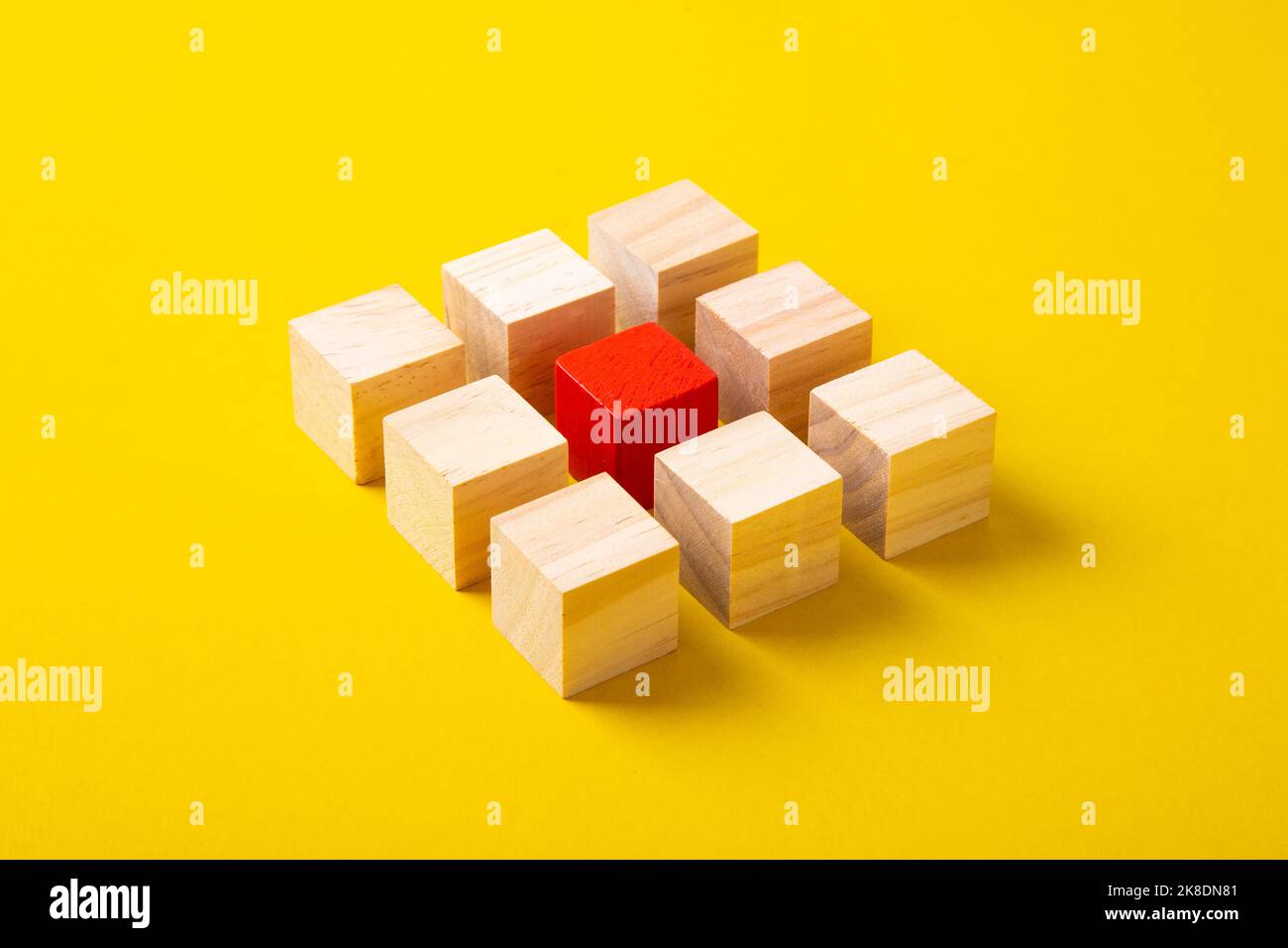 Blocco di legno rosso che si erge fuori dal gruppo blocchi di legno su sfondo giallo. Foto Stock