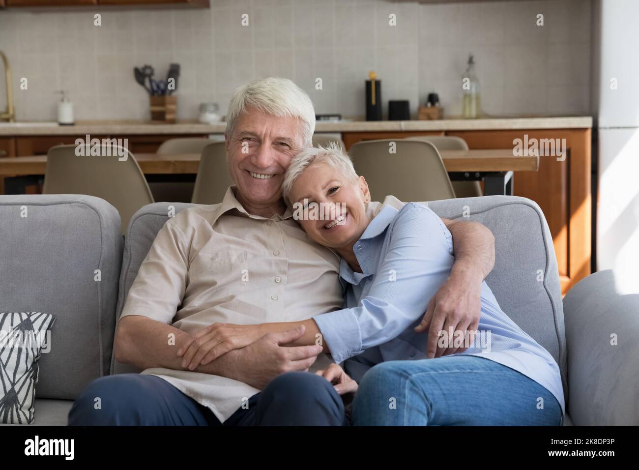 Amando la coppia più anziana che abbraccia rilassarsi sul divano guardando la macchina fotografica Foto Stock