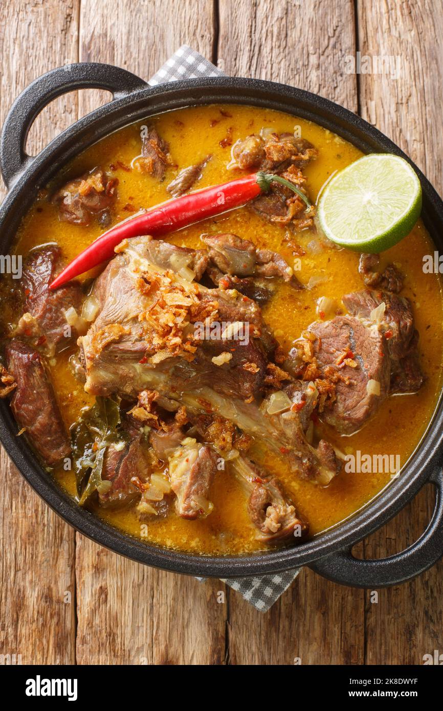 Curry di agnello o indonesiano Gulai Kambing per Eid closeup sulla padella sul tavolo di legno. Vista verticale dall'alto Foto Stock