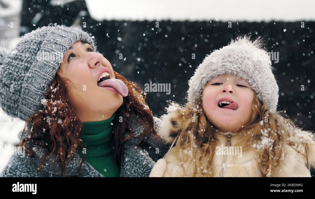 divertimento invernale per tutta la famiglia. cattura i fiocchi di neve con la lingua. Famiglia felice, madre e figlia stanno interferendo i fiocchi di neve con le loro lingue, godendosi della neve e della caduta di neve, avendo divertimento, spendendo insieme il tempo in giorno di inverno nevoso. Slow motion. Foto di alta qualità Foto Stock