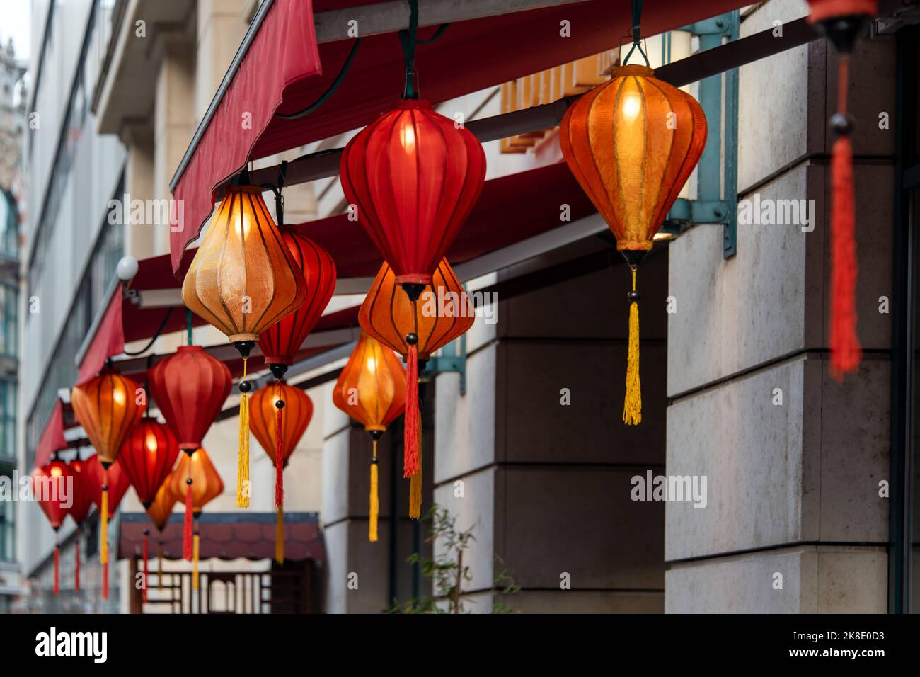 Lanterne cinesi rosse che pendono all'aperto come ghirlande. Lanterne tradizionali asiatiche decorative e luminose per ristoranti, caffè o case. Simboli di ricchezza, Fam Foto Stock