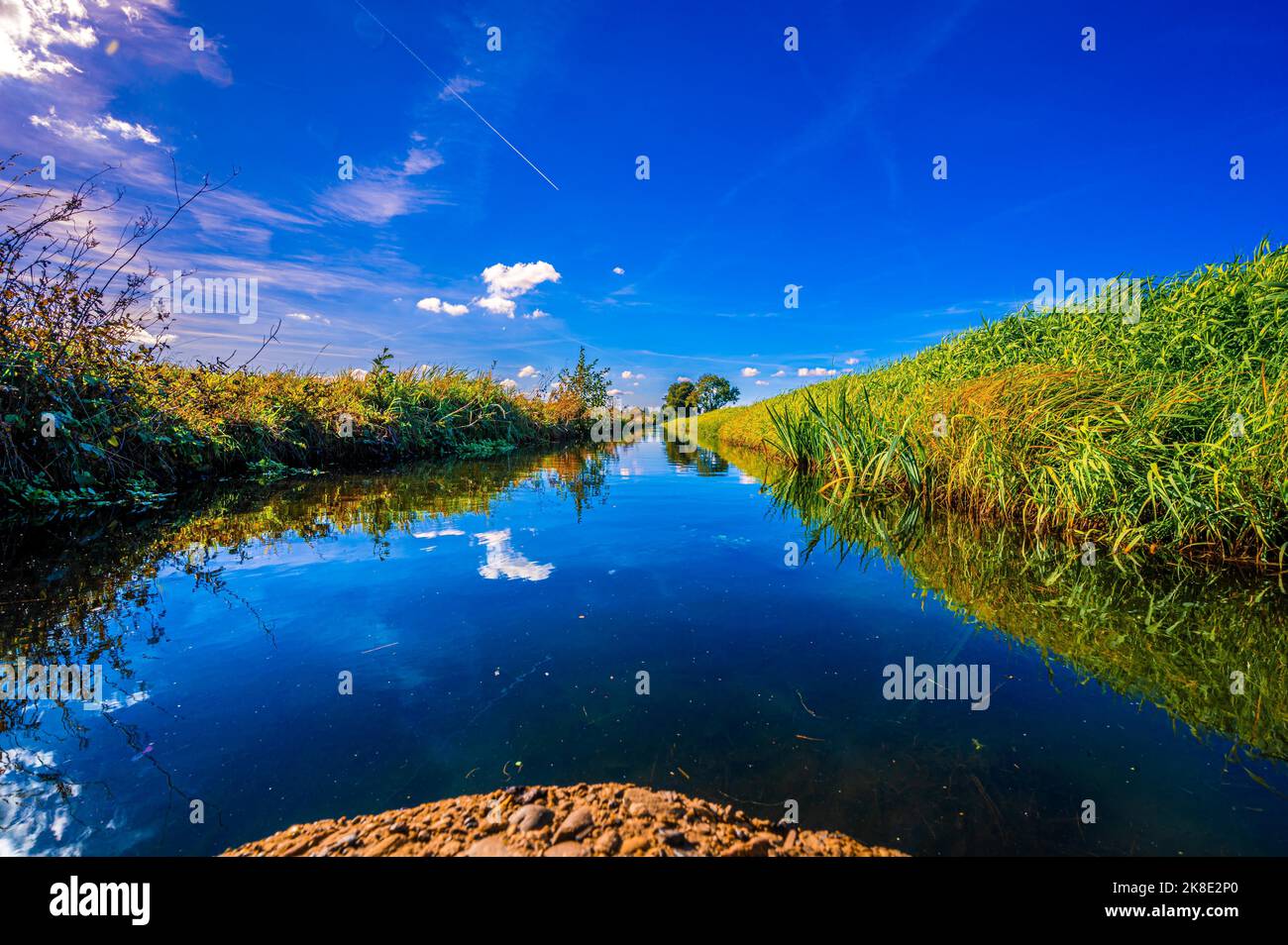 Un piccolo canale di irrigazione tra due campi con riflesso di nuvole e il cielo blu in autunno, Hagenburg, bassa Sassonia, Germania Foto Stock