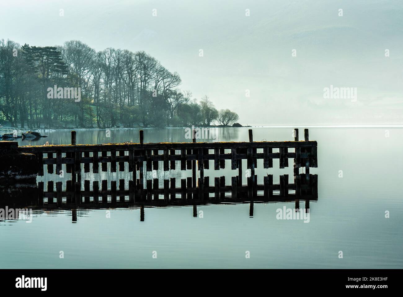 Un vecchio molo in disuso si riflette in Ullswater in una tranquilla e tranquilla primavera mattina. Lake District, Cumbria, Inghilterra Foto Stock