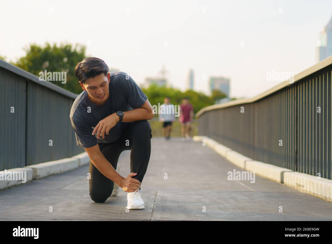 Asian Runner che subisce lesioni alla caviglia dopo lo sport all'aperto in un parco della periferia della città Foto Stock