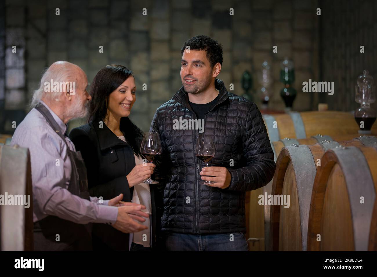 L'enologo guida e ospita una giovane coppia caucasica durante il tour della cantina, una cantina con una lunga tradizione produttiva Foto Stock