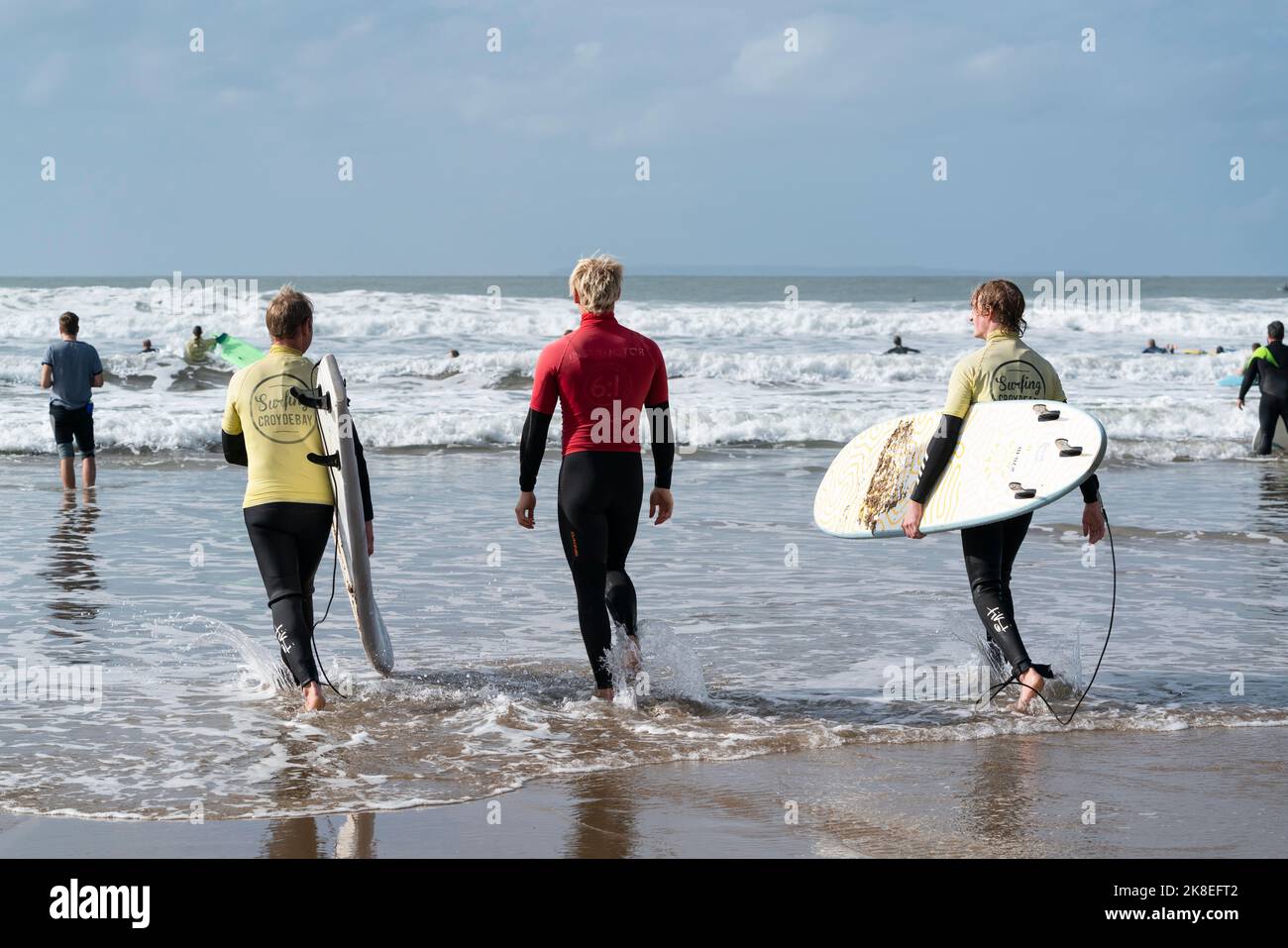 Due surfisti si dirigono verso le onde a Croyde Bay, North Devon, Regno Unito, con un istruttore (centro) di una scuola di surf locale. Foto Stock