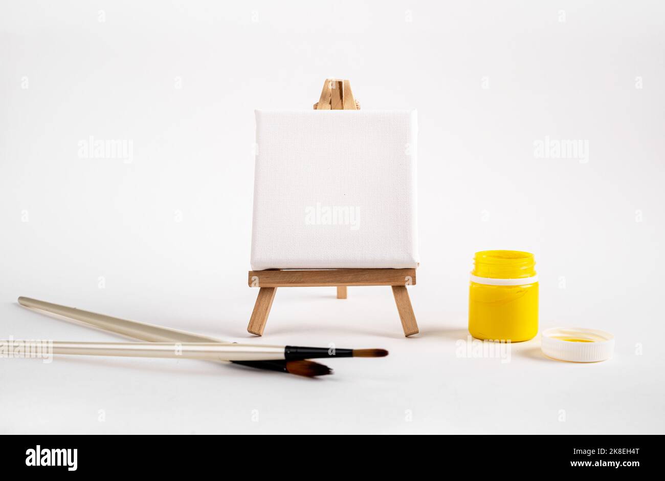 Mockup quadro in tela su treppiede in legno con pennelli da disegno e barattolo di vernice gialla. Foto di alta qualità Foto Stock