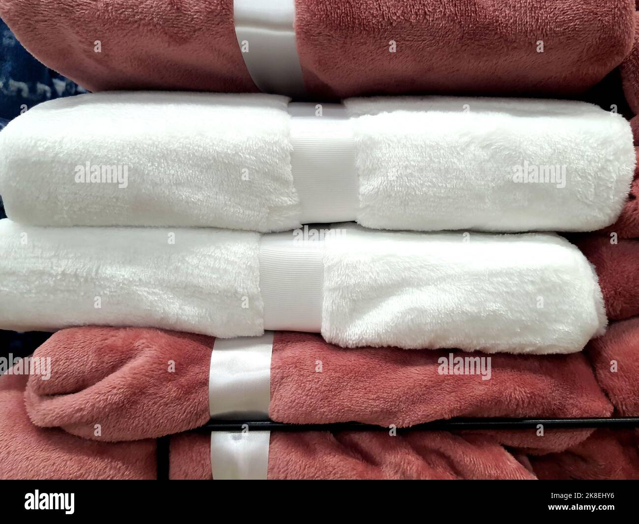 Una pila di coperte calde, copriletto, si trova sullo scaffale del negozio. Articoli per la casa, morbidi, soffici in supermercato, rosa e bianco Foto Stock