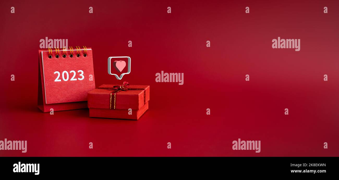 3d amore come il cuore icone galleggianti su piccolo regalo rosso presente scatola con 2023 anno di scrivania calendario su sfondo rosso con spazio copia. Banner regalo speciale Foto Stock