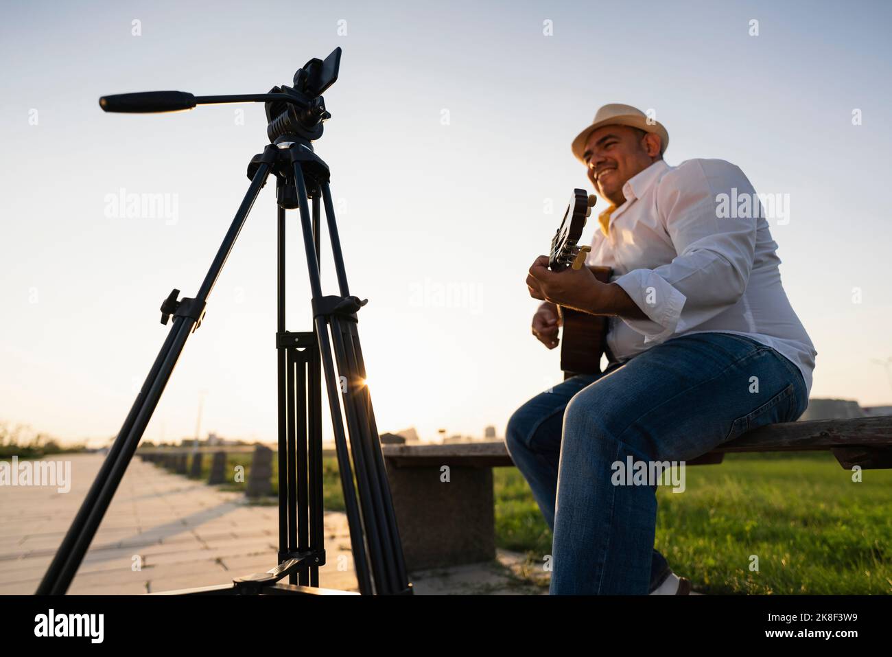 Sorridente musicista di strada che suona la chitarra e registra tramite smartphone su treppiede Foto Stock