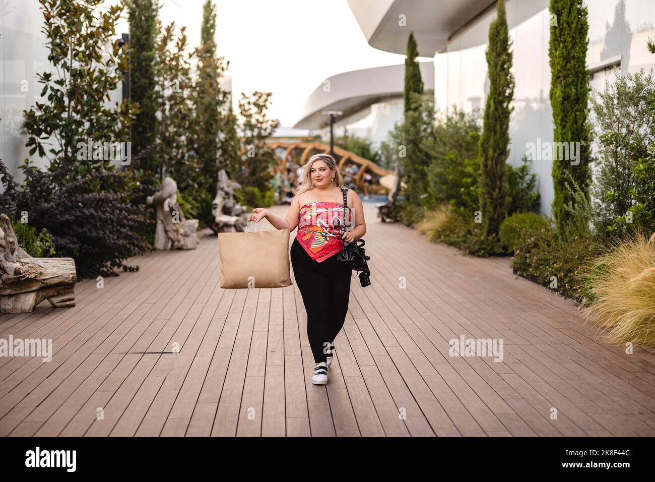 Giovane donna sorridente che trasporta la borsa di shopping che cammina sul sentiero Foto Stock