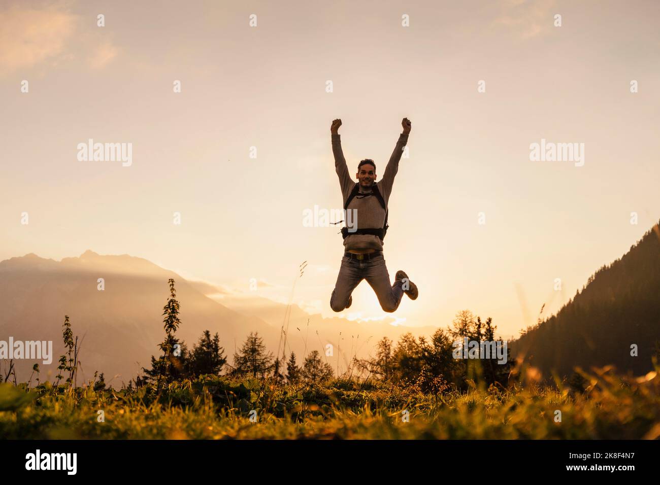 Uomo felice che salta in cima alla montagna al tramonto Foto Stock