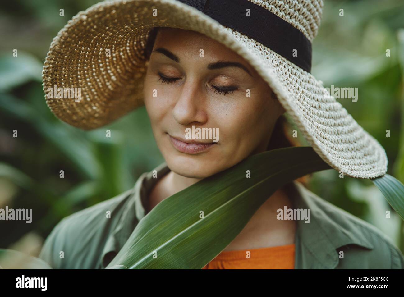 Donna matura con occhio chiuso che tocca foglia verde sul viso in giardino Foto Stock