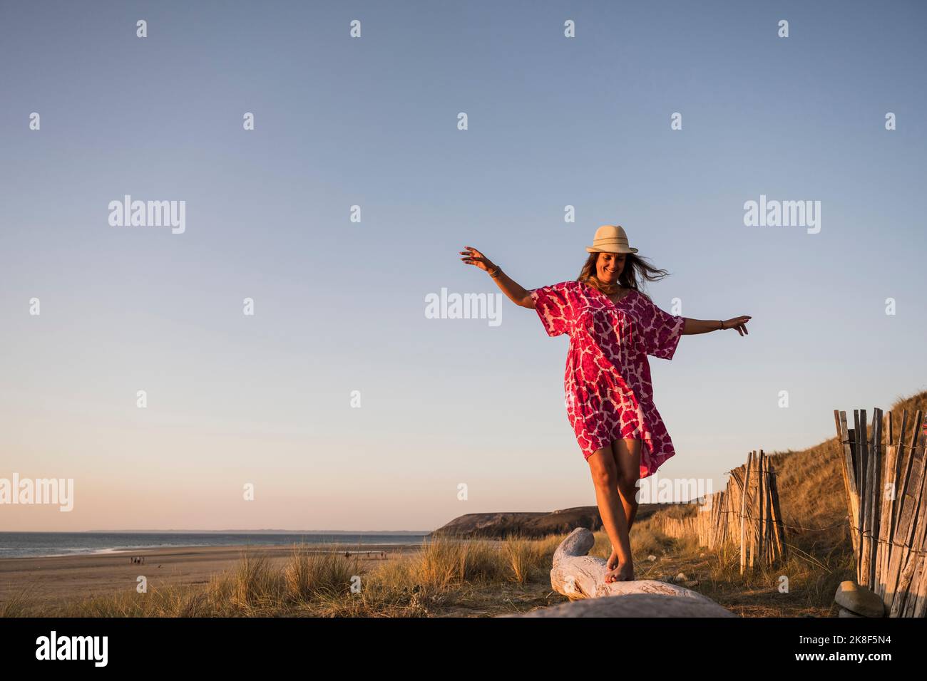 Donna matura felice con le braccia fuori teso a piedi sul log in spiaggia Foto Stock