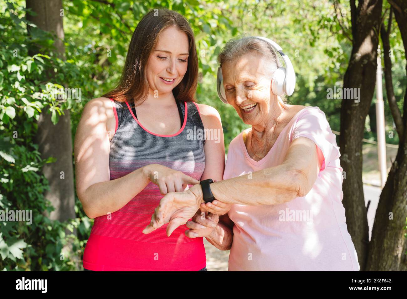 Sorridente istruttore di fitness che insegna un orologio intelligente alla donna anziana al parco Foto Stock