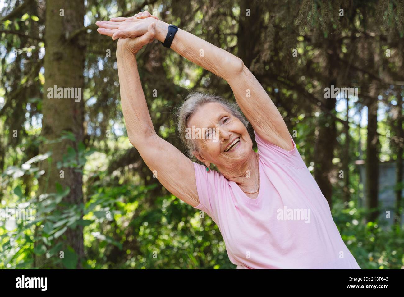 Donna anziana felice con le braccia alzate esercizio di stretching pratica al parco Foto Stock