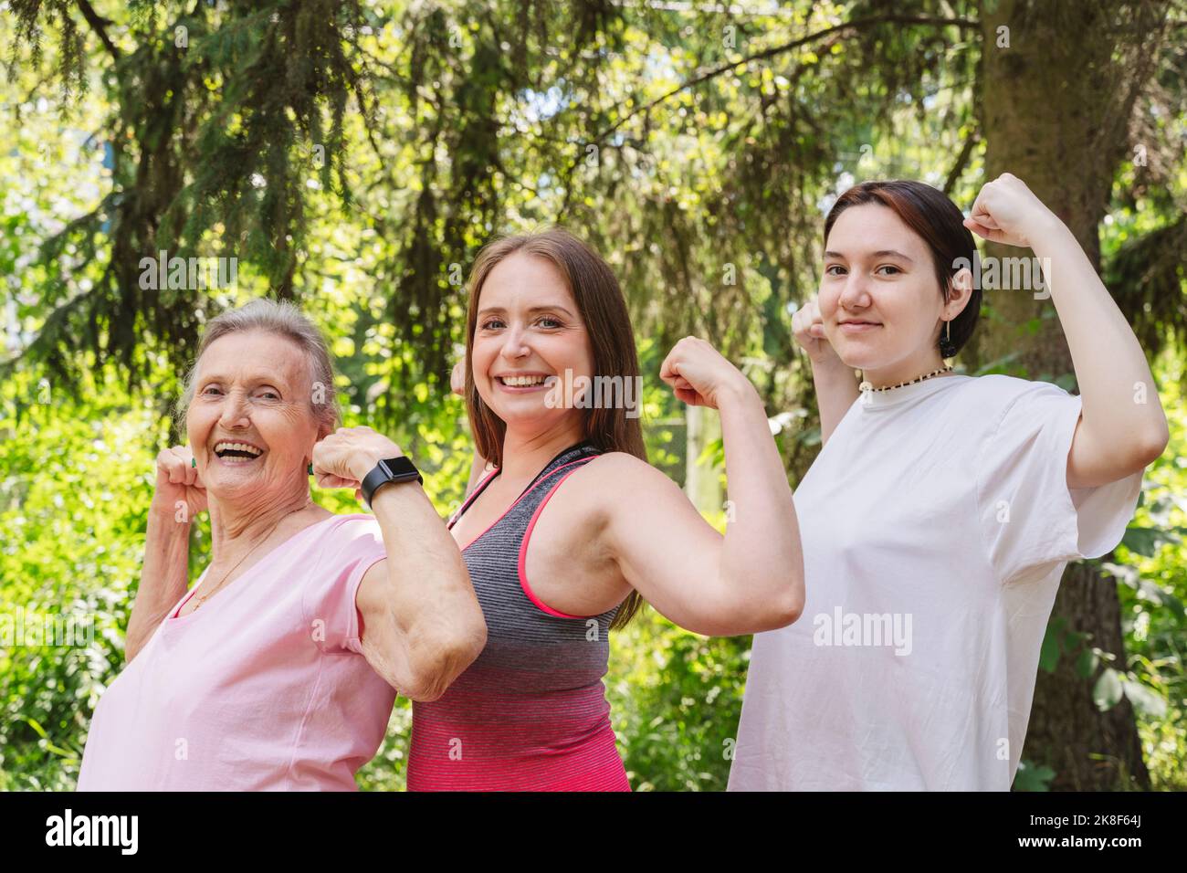 Donna anziana attiva che flette i muscoli con la figlia e la nipote al parco Foto Stock Donna anziana attiva che flette i muscoli con la figlia e la nipote al parco Foto Stock