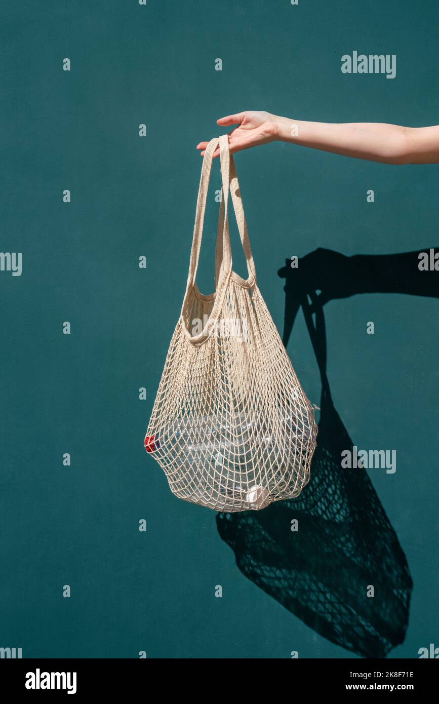 Mano di donna che tiene il sacchetto della rete con le bottiglie di plastica davanti alla parete Foto Stock