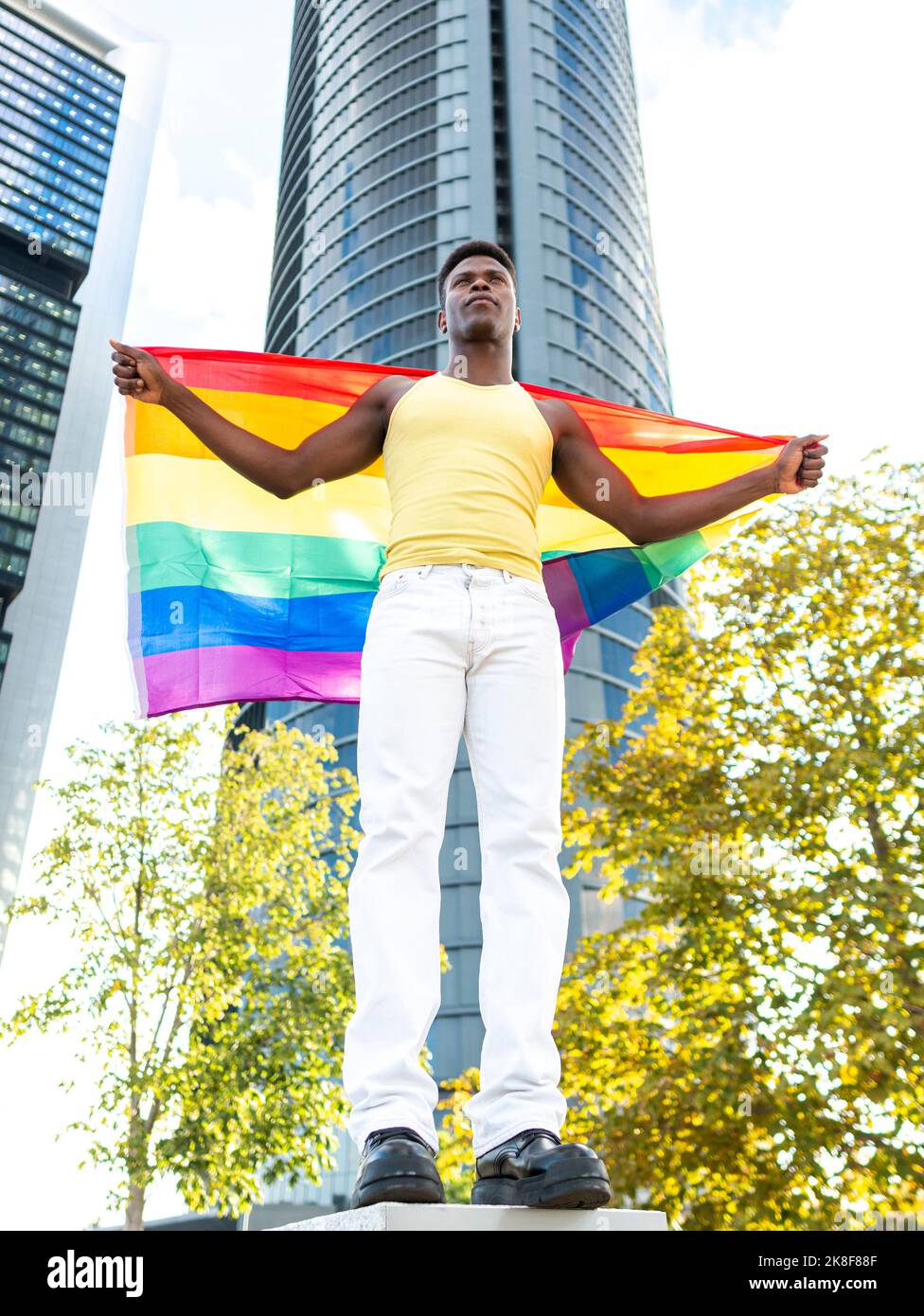 Uomo con bandiera arcobaleno di fronte al moderno grattacielo Foto Stock