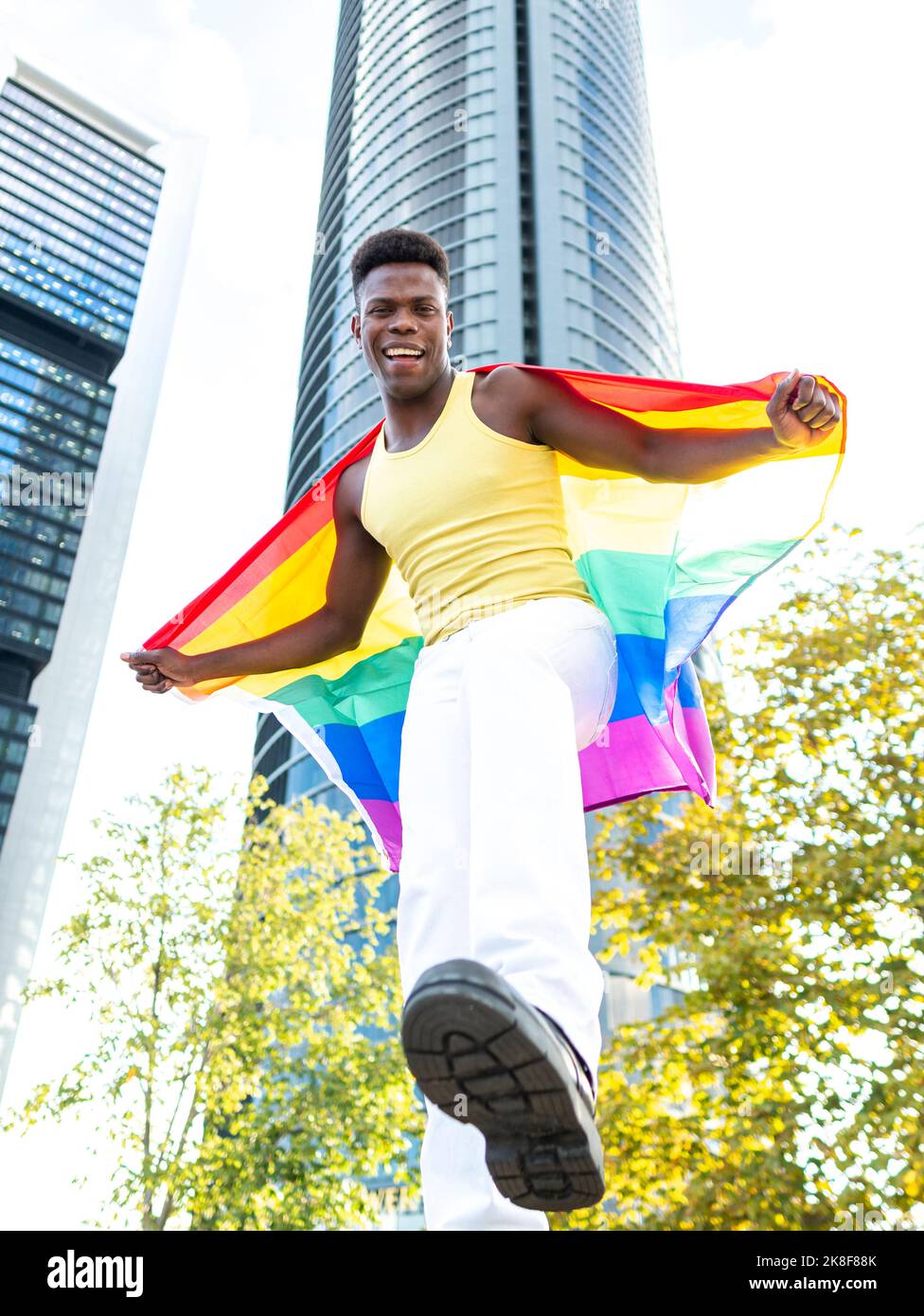 Felice uomo con bandiera arcobaleno di fronte al moderno grattacielo Foto Stock