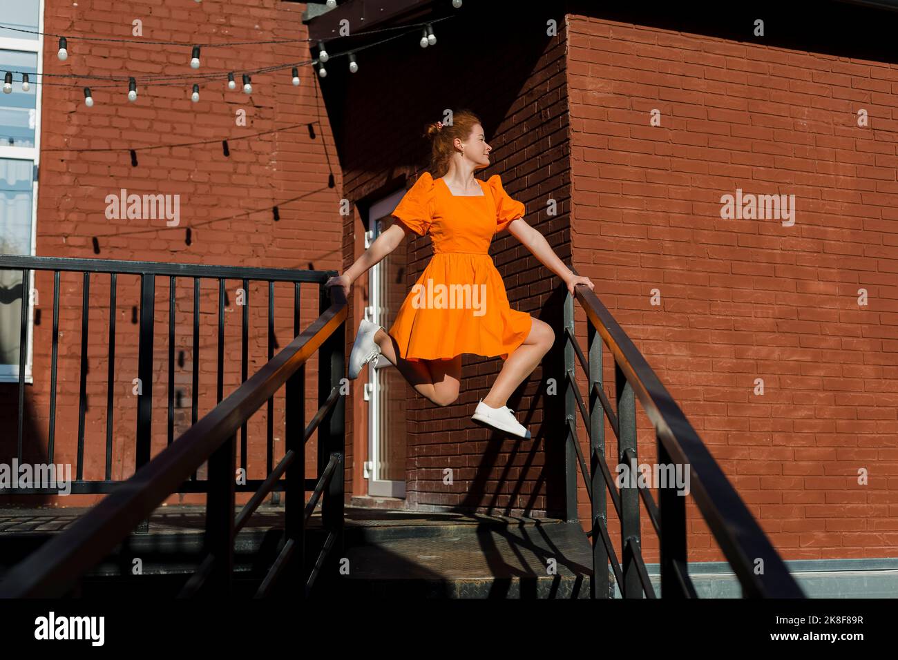 Donna in abito arancione bilanciamento su ringhiere di scala Foto Stock