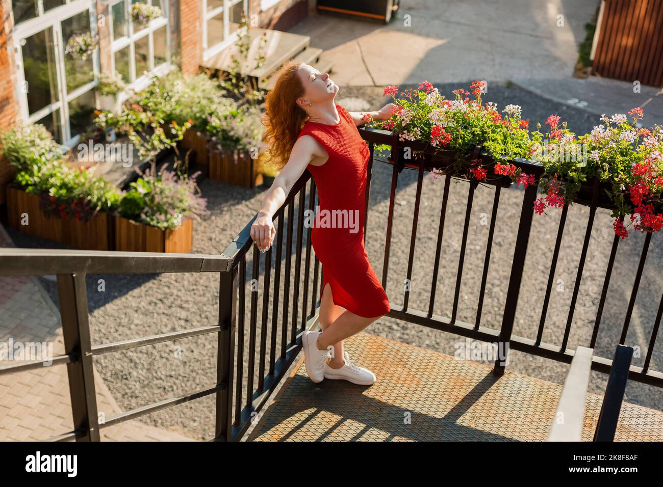 Donna che indossa un abito rosso con gli occhi chiusi appoggiandosi sulla ringhiera Foto Stock