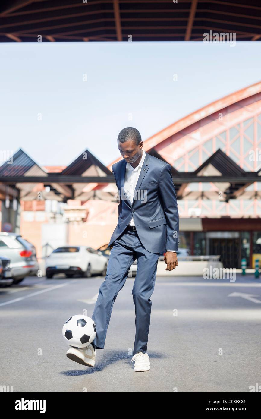 Giovane uomo d'affari che gioca con la palla di calcio al parcheggio nelle giornate di sole Foto Stock