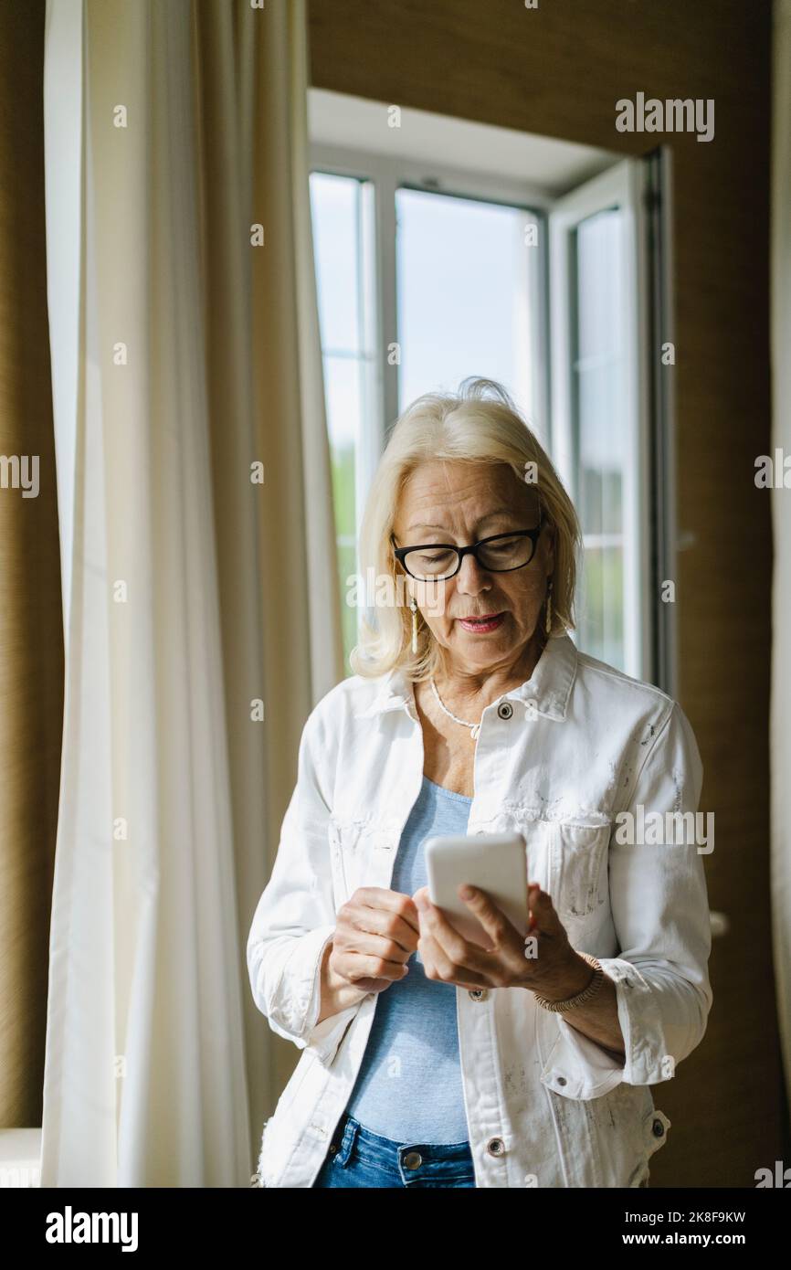 Donna Senior per la messaggistica di testo attraverso smart phone a casa Foto Stock