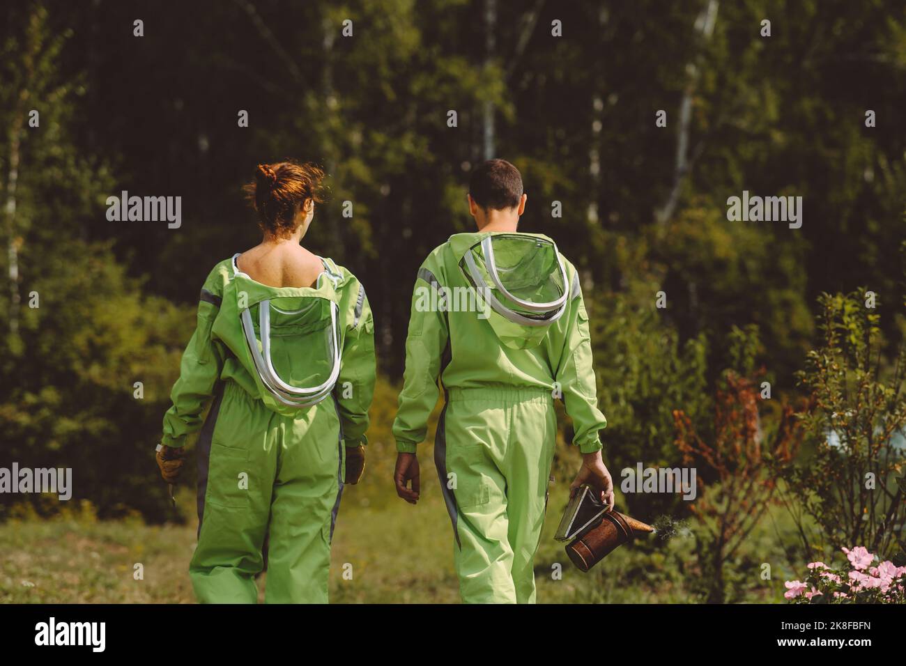 Apicoltori che indossano tute protettive che camminano insieme all'apiario Foto Stock