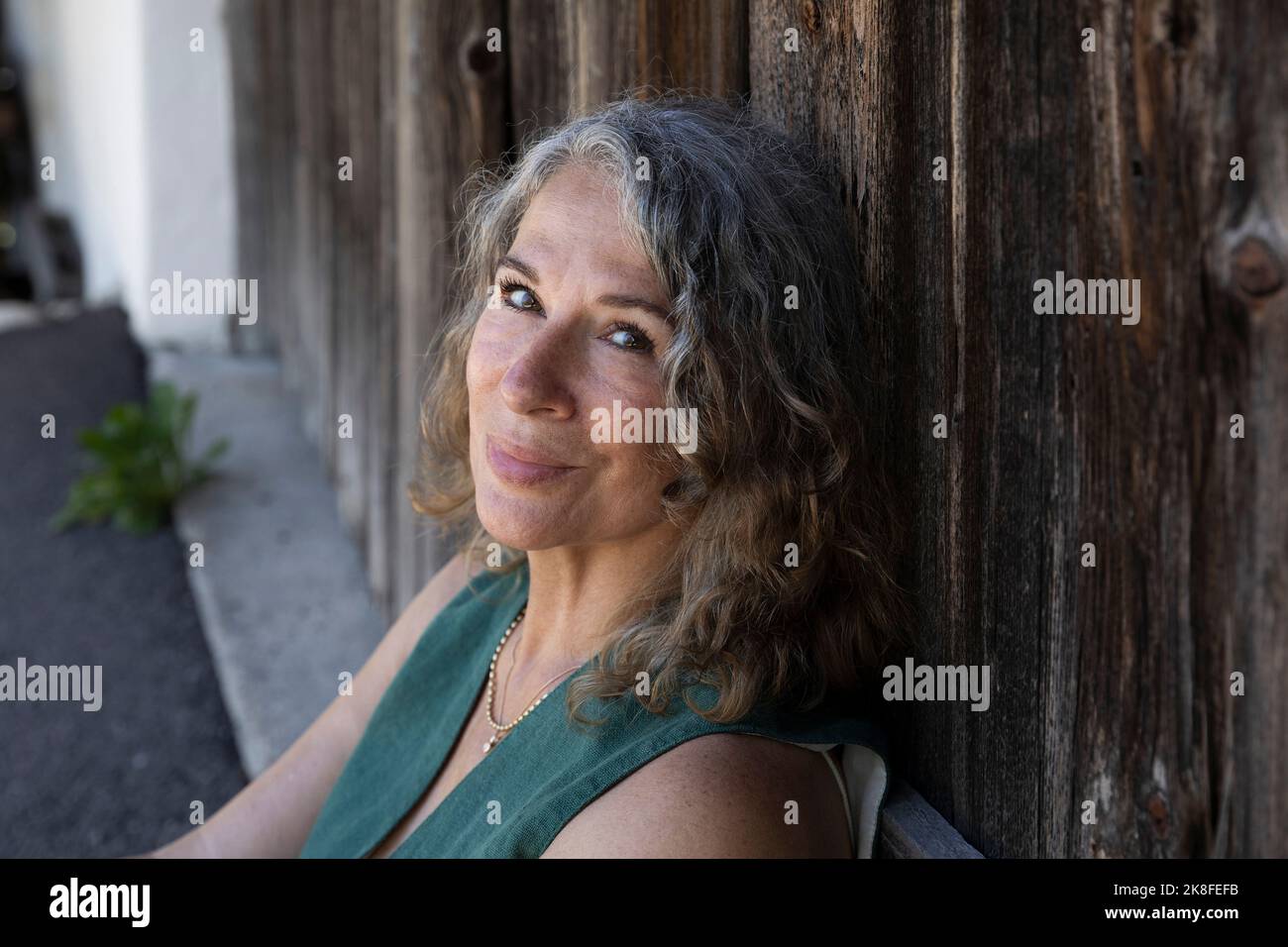 Donna sorridente dai capelli grigi appoggiata su una porta di legno Foto Stock