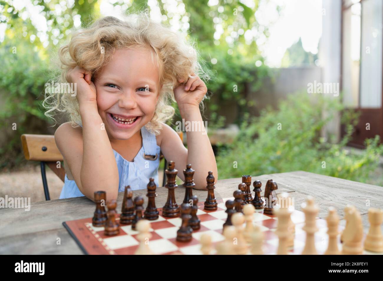 Ragazza bionda felice seduta con scacchiera in giardino Foto Stock