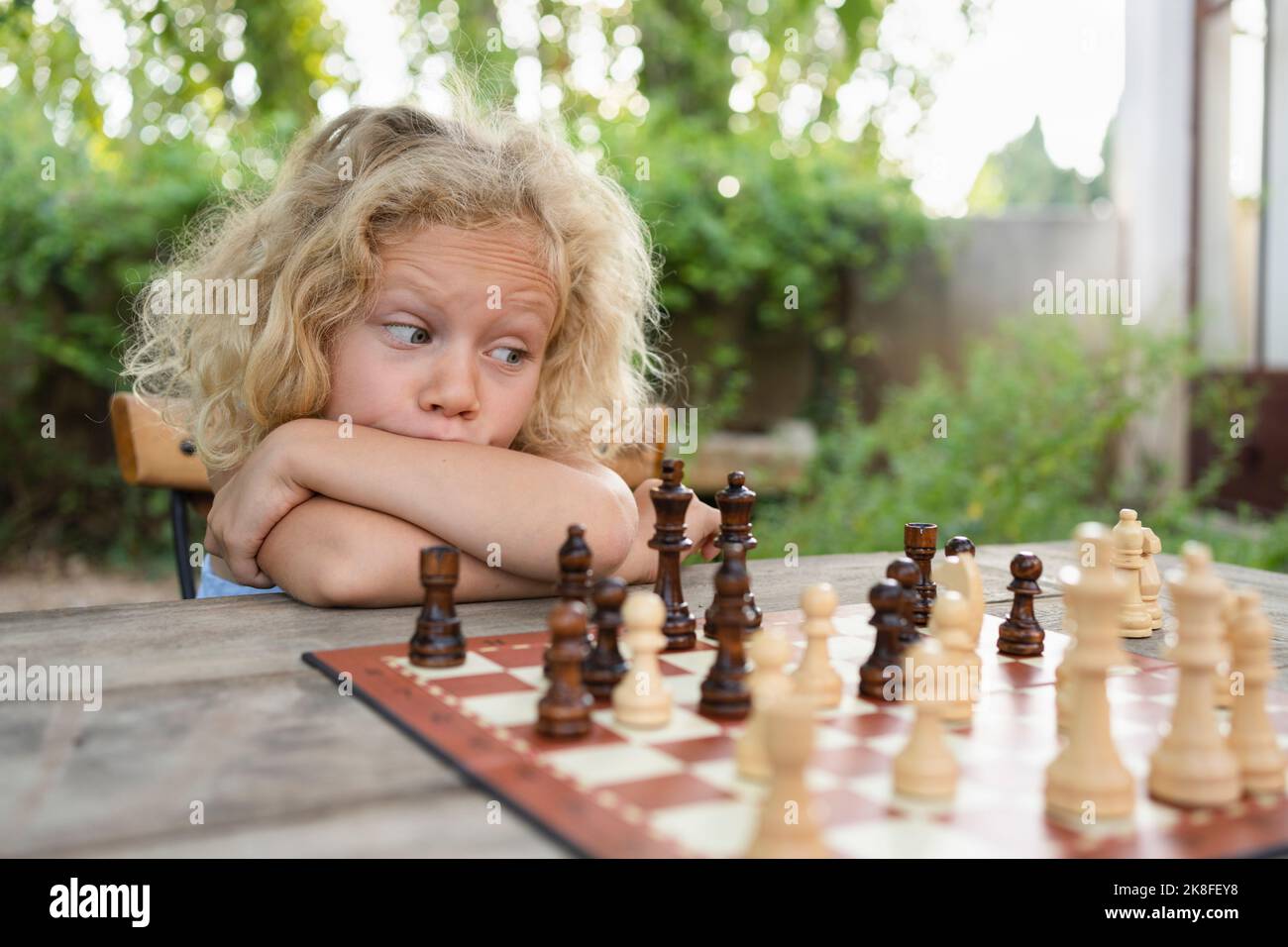 Ragazza premurosa con capelli biondi guardando scacchiera sul tavolo Foto Stock